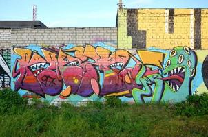 Abstraktes buntes Fragment von Graffiti-Gemälden auf alter Ziegelwand mit gruseligem Oktopus-Gesicht. Straßenkunstkomposition mit Teilen ungeschriebener Briefe und Zeichentrickfigur foto