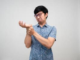 asiatischer männlicher mitarbeiter, der eine brille trägt, fühlt schmerzen am handgelenk wegen des hart arbeitenden bürosyndroms isoliert foto
