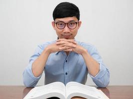 gutaussehender asiatischer geschäftsmann trägt eine brille, die selbstbewusst auf sie schaut und am schreibtisch sitzt foto