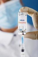 eine Ampulle mit der Aufschrift Virusimpfstoff und eine Spritze in den Händen eines wissenschaftlichen Arztes in Gummihandschuhen mit einer Impfstoffnahaufnahme.