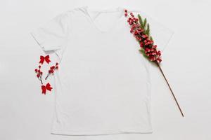 schließen sie herauf weißes leeres schablonen-t-shirt mit kopienraum und weihnachtsfeiertagskonzept. Draufsichtmodellt-shirt und rote Feiertagsdekorationen auf weißem Hintergrund. frohes neues jahr zubehör. Weihnachts-Outfit foto