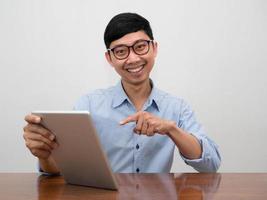 positiver geschäftsmann, der eine brille trägt, zeigt mit dem finger auf das tablet in der hand mit einem glücklichen lächeln foto