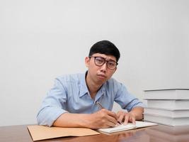 asiatischer geschäftsmann, der eine brille trägt, sitzt am arbeitstisch und fühlt sich versucht foto