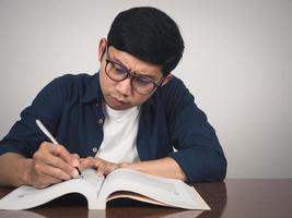 Mann trägt eine Brille ernsthaftes Studium Lehrbuch auf dem Tisch foto