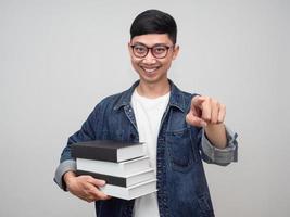 Porträt junger Mann trägt eine Brille Jeanshemd hält die Bücher glückliches Lächeln zeigt mit dem Finger auf Sie isoliert foto