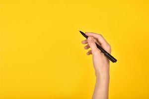 Mädchenhand mit einem Stift auf gelbem Hintergrund. Werbeaufschrift. foto