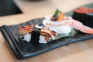 Selektiver Fokus auf Gänseleber-Sushi mit einer Unschärfe von anderem Sushi auf der rechteckigen schwarzen Keramikplatte.