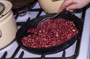 Braten von Erdnüssen, die Hand einer Frau, die Erdnüsse in einer Bratpfanne rührt, Nahaufnahme. foto