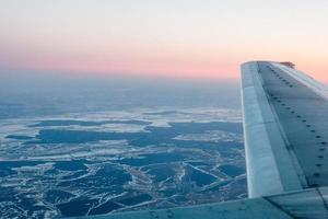 rosa Sonnenuntergang von oben, über Wintergelände und Flugzeugflügel foto