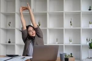 asiatische geschäftsfrau streckt ihre arme aus, um ihre müden muskeln zu entspannen, nachdem sie den ganzen tag an ihrem schreibtisch im büro gearbeitet hat. foto