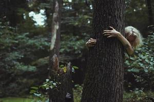 blonde Frau, die sich hinter alter Baumlandschaftsfotografie versteckt foto