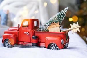 Rotes Retro-Auto mit einem Weihnachtsbaum schmückt mit dem Hausschlüssel im Pickup-Truck zu Weihnachten. Hauskauf, Umzug, Hypothek, Darlehen, Immobilien, Feststimmung, Neujahr