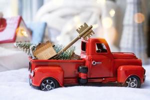 Rotes Retro-Auto mit einem Weihnachtsbaum schmückt mit dem Hausschlüssel im Pickup-Truck zu Weihnachten. Hauskauf, Umzug, Hypothek, Darlehen, Immobilien, Feststimmung, Neujahr