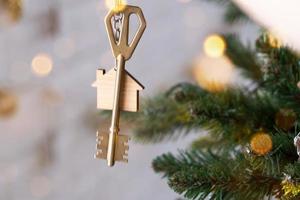 schlüssel zum haus mit einem schlüsselbund hängt am weihnachtsbaum. ein geschenk für neujahr, weihnachten. Bau, Design, Projekt, Umzug in ein neues Haus, Hypothek, Miete und Kauf von Immobilien. Platz kopieren