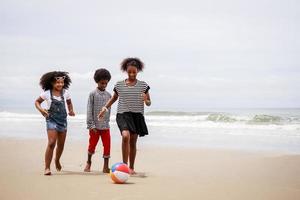 Eine Gruppe afroamerikanischer Kinder spielt Ball an einem tropischen Strand. ethnisch vielfältiges Konzept