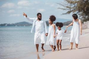 afroamerikanische familie, die im urlaub zusammen am strand spazieren geht und spaß an einem tropischen strand hat foto