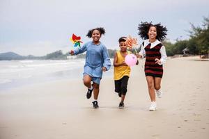 glückliche gruppe afroamerikanischer kinder, die es genießen, mit spielzeug am strand zu rennen foto