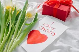 frauentag, muttertagskonzept. weiße tulpen, geschenkgeschenk, grußkarte mit text ich liebe mama foto