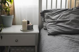 Schlafzimmer mit hellem Interieur. Moderne Kerze, heimische Pflanze auf dem Nachttisch neben dem Bett. Zuhause Aroma