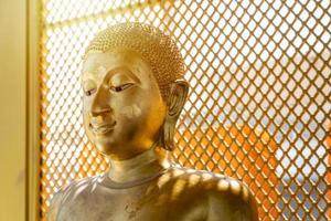Vintage goldene Buddha-Statue vor gelb-orangeem Grillhintergrund mit dem quadratischen Musterlicht von hinten.