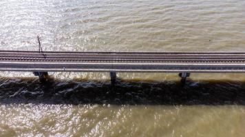 luftaufnahme eines erstaunlichen reisezuges, der auf einer schwimmenden eisenbahnbrücke über dem wasser des sees in pa sak jolasid dam mit blauem himmel in lopburi, thailand, geparkt ist. foto