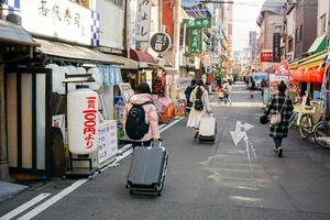 osaka, japan, 2019 - gruppe chinesischer touristen, die gepäck zur u-bahn in der städtischen stadt osaka laufen und schleppen, um dringend zum flughafen zu gelangen. foto