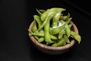 Edamame-Bohnen-Salat mit Meersalz, serviert in einer dunklen Schüssel. isoliert auf schwarzem Hintergrund. Essen im Restaurant. japanische küche foto