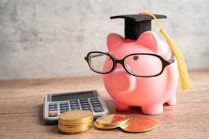 Sparschwein mit Brille mit Münzen und Abschlusshut Sparschwein Bildungskonzept. foto