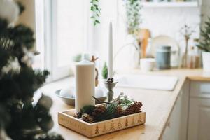 weihnachtskomposition aus weißen kerzen, tannenzweigen und kegeln in der küchenecke zu hause foto