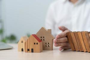 Versicherungen mit Händen schützen ein Haus. Der hölzerne Dominostein fällt gleich auf das Haus. hausversicherung oder hausversicherungskonzept foto