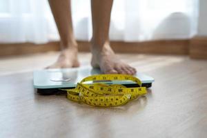 Frauen stehen auf elektronischen Waagen mit Messkabeln, die eine Gewichtskontrolle erfordern. Frauenfuß treten auf Waagen mit Maßband. Diät-Konzept foto