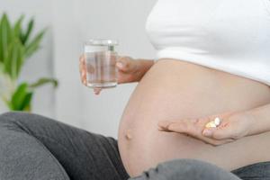 Schwangere nehmen Vitamine und Trinkwasser, um ungeborene Kinder zu ernähren. Durch die Einnahme von Medikamenten oder Vitaminen müssen schwangere Frauen die für die körperliche Entwicklung erforderliche Ernährung aufrechterhalten. nähren, notwendig. foto