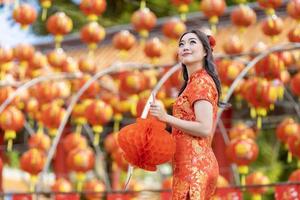 asiatische frau im roten cheongsam qipao kleid, das laterne hält, während sie den chinesischen buddhistischen tempel während des neuen mondjahres für traditionelles kulturkonzept besucht foto