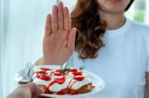 Junge Frau benutzt die Hand, um den Teller mit Gebäck zu schieben, weigert sich, Mehl und Zucker zu essen, um Gewicht zu verlieren. foto