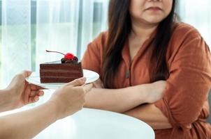 Dicke Frau schiebt den Teller auf einen Schokoladenkuchen. Absicht, Gewicht für eine gute Gesundheit und eine gute Form zu verlieren foto