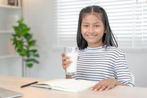 Kinderfrauen trinken Milch, um den Körper zu ernähren und das Gehirn zu ernähren. asiatische junge kleine Mädchen lernen zu Hause. mädchen trinken gerne milch und lesen ein buch für die prüfung, homeschool. Bildung, Vitamine, Entwicklung