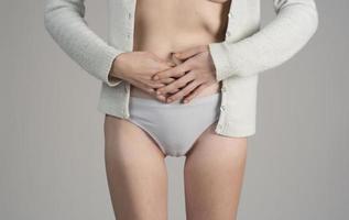 Junge schöne Frau in schmerzhaftem Ausdruck, die ihren Bauch hält und unter Menstruationsschmerzen leidet, liegt traurig auf dem Heimbett und hat Bauchkrämpfe im weiblichen Gesundheitskonzept foto