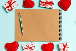 Draufsicht auf Bastelnotizbuch, umgeben von Herzen und Geschenkboxen auf buntem Hintergrund. Valentinstag foto