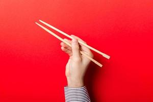 Die Hand des Jungen zeigt Essstäbchen auf rotem Hintergrund. asiatisches küchenkonzept mit leerem raum für ihr design foto