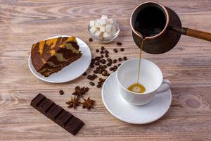 Draufsicht auf eine Tasse Kaffee und ein Stück leckeren Kuchen auf einer Untertasse, Kaffeebohnen, eine Schüssel mit Zuckerwürfeln, Schokoriegel und Anis auf hellem Holztisch foto