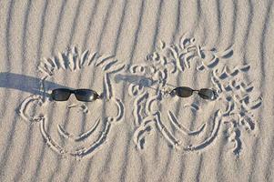 Gesicht in den Sand am Strand gezeichnet, mit Sonnenbrille. Sand mit Wellenmuster foto