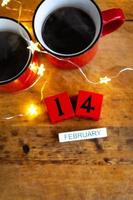 zwei tassen kaffee in roten tassen auf einem hintergrund von girlanden. Postkarte mit Datum und Monat. Morgenfrühstück zum Valentinstag. von oben betrachten. foto