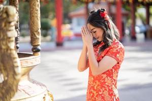 eine junge asiatische frau, die traditionelles cheongsam qipao kostüm trägt, das für den besten wunschsegen und viel glück im chinesischen buddhistischen tempel betet. foto