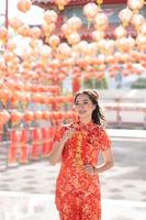 frohes chinesisches neujahr. junge asiatische frau, die traditionelles cheongsam qipao kleid trägt, das segensvermögenskarte im chinesischen buddhistischen tempel hält. chinesischer text bedeutet gesegnet von einem glücksstern. Emotion Lächeln foto