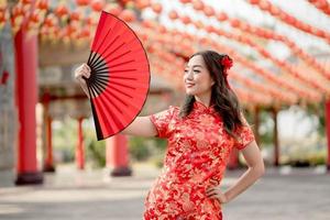 schöne dame, die traditionelles cheongsam qipao kostüm trägt, das fan im chinesischen buddhistischen tempel hält. Konzept des chinesischen Neujahrsfestes foto