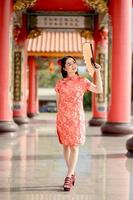 vertikales Bild. frohes chinesisches neujahr. schöne asiatische frau, die traditionelles cheongsam qipao-kleid trägt, das fan hält, während sie den chinesischen buddhistischen tempel besucht foto