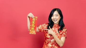 junge Frau in traditionellem Cheongsam-Qipao-Kostüm, die die Segenskarte isoliert auf rotem Hintergrund hält und zeigt. chinesischer text bedeutet viel glück, großer gewinn foto