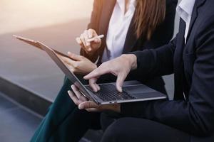 asiatischer geschäftsmann und junge schöne frau, die an einem digitalen tablet-computer arbeiten, der außerhalb des bürogebäudes steht. foto