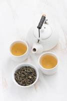 Teekanne und Tassen grüner Tee auf weißem hölzernem Hintergrund foto