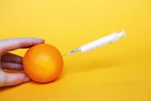 Orangenfrüchte mit Spritze, die Flüssigkeit mit Vitamin C extrahiert. natürliches anti-aging-kosmetikkonzept